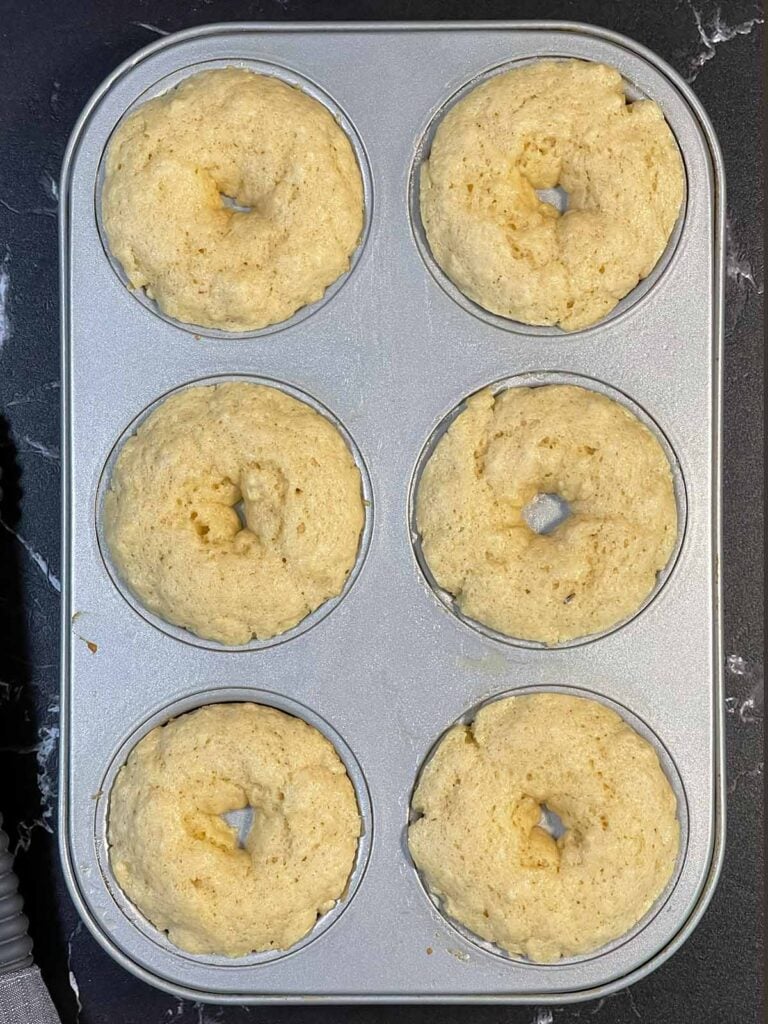 Freshly baked donuts in a donut pan, lightly golden and risen.