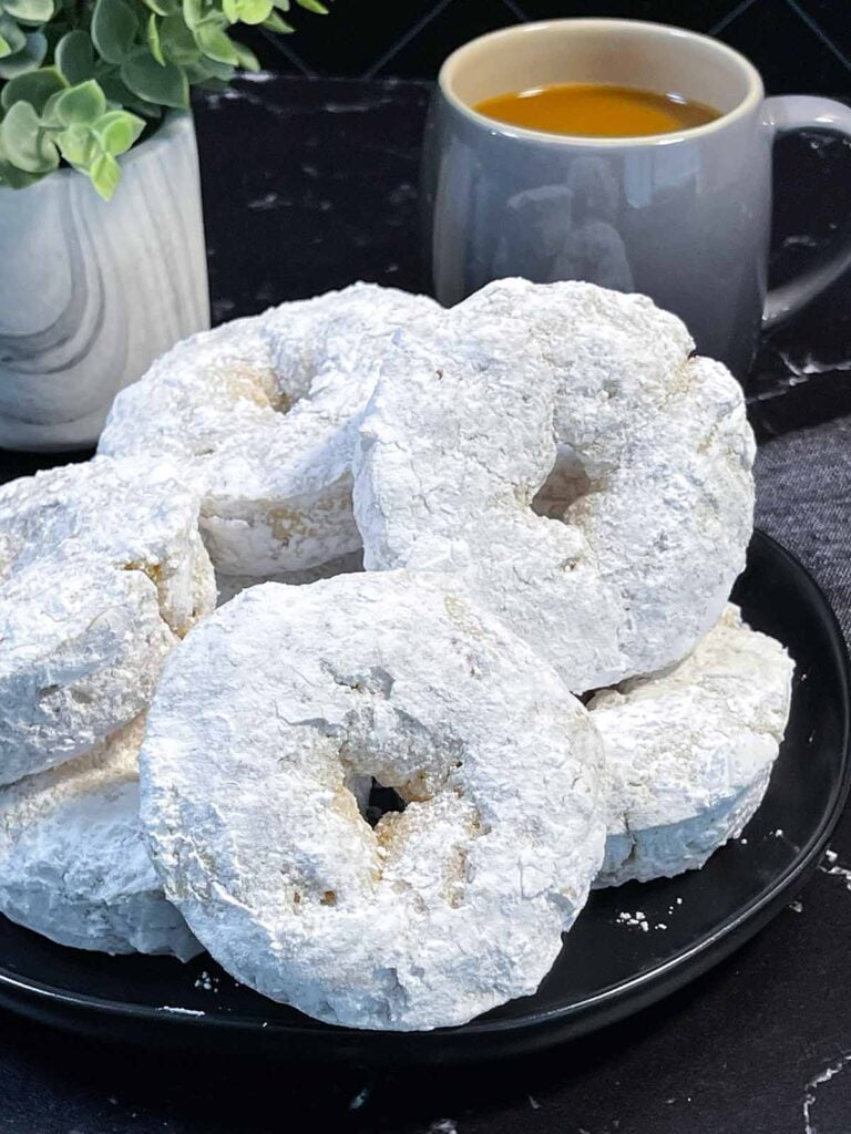 Baked powdered sugar donuts stacked on a plate.
