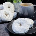Powdered sugar coated baked donuts stacked on a plate with a soft, cake-like texture.