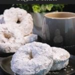 Baked powdered sugar donuts stacked on a plate.