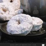 Baked powdered sugar donuts stacked on a plate.
