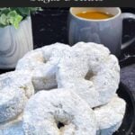 Baked powdered sugar donuts stacked on a plate.