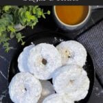 Baked powdered sugar donuts stacked on a plate.