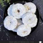 Baked powdered sugar donuts stacked on a plate.