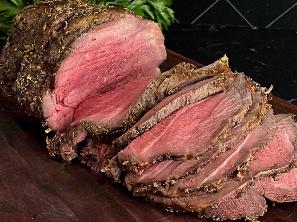 Sliced beef sirloin tip roast cooked medium rare on a wooden cutting board