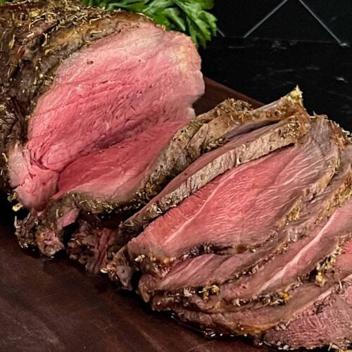 Sliced beef sirloin tip roast cooked medium rare on a wooden cutting board