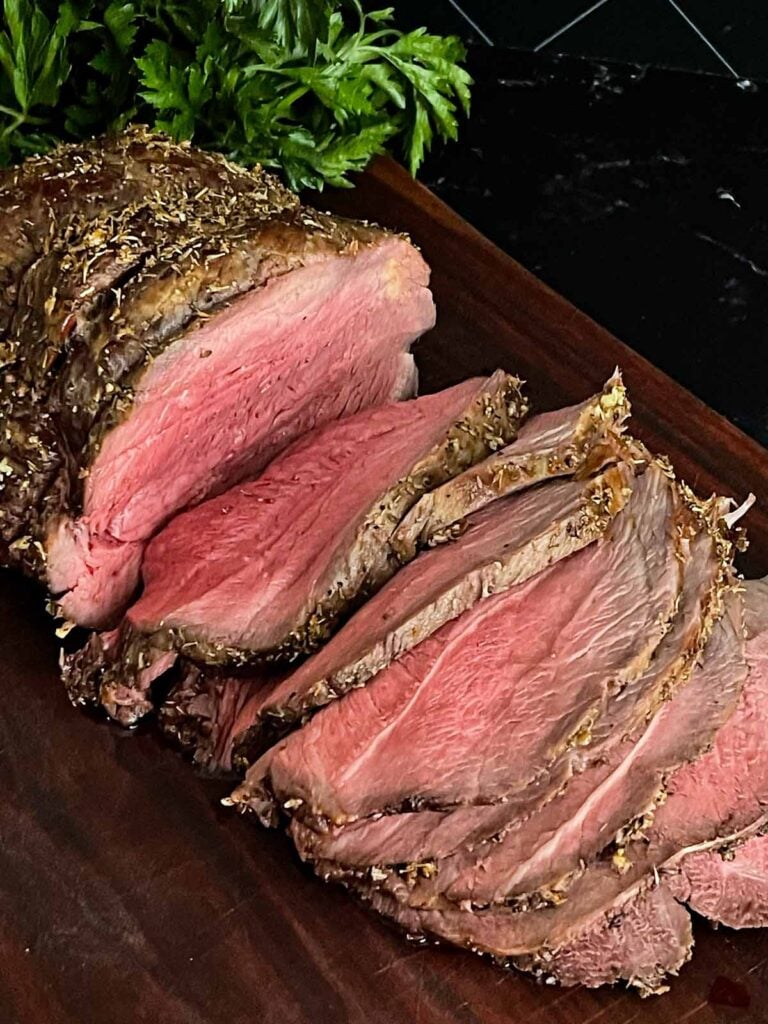 Sliced beef sirloin tip roast cooked medium rare on a wooden cutting board