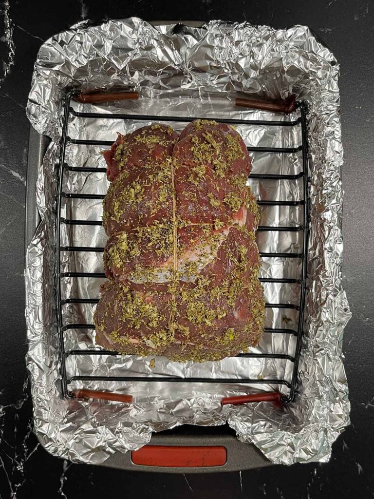 Garlic herb coated beef sirloin tip roast on a roasting rack before roasting.