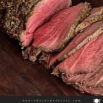 Sliced beef sirloin tip roast cooked medium rare on a wooden cutting board