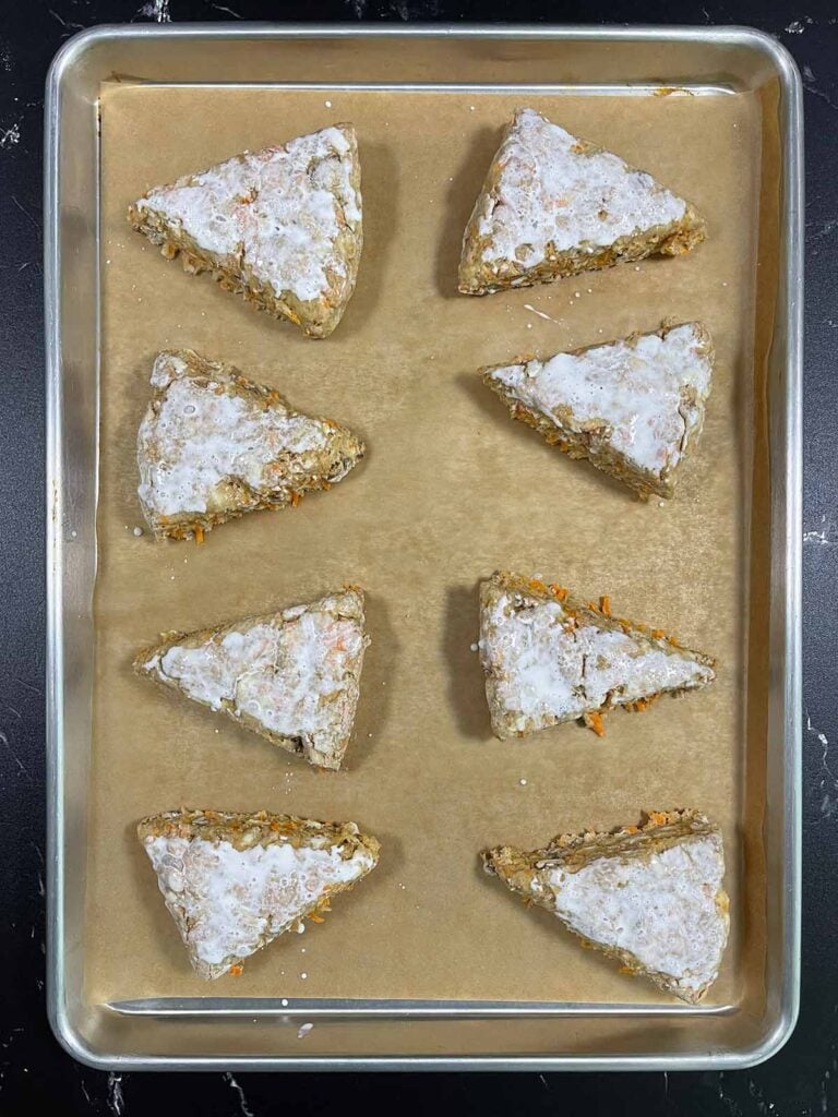 Raw carrot cake scones on a parchment paper lined baking sheet before going into the oven.