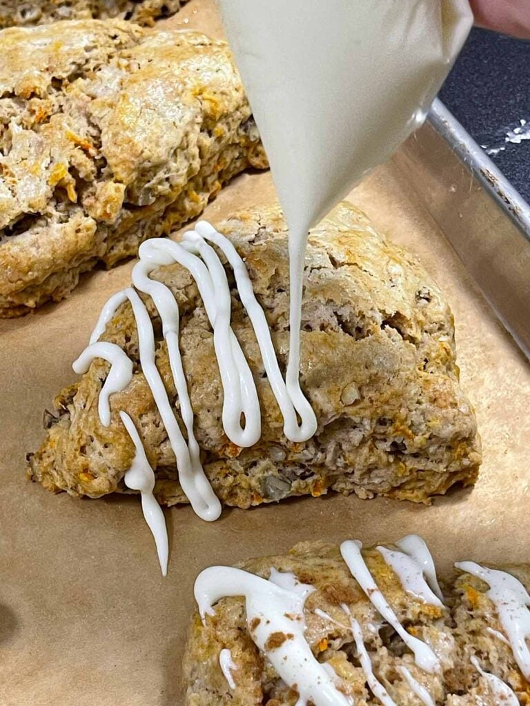 Cream cheese icing being piped over each carrot cake scone.
