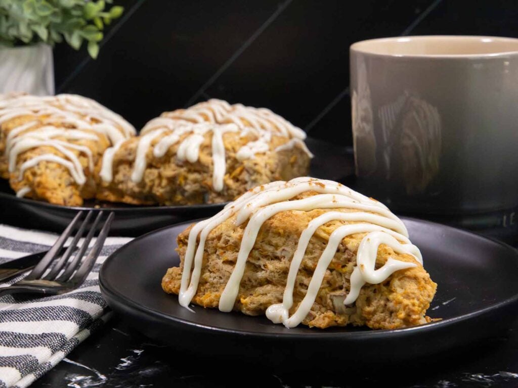 Bakery-style carrot cake scones topped with cream cheese glaze on a plate, made with fresh carrots, warm spices, and chopped pecans.