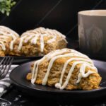 Bakery-style carrot cake scones topped with cream cheese glaze on a plate, made with fresh carrots, warm spices, and chopped pecans.