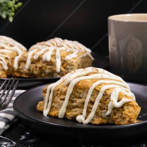 Bakery-style carrot cake scones topped with cream cheese glaze on a plate, made with fresh carrots, warm spices, and chopped pecans.