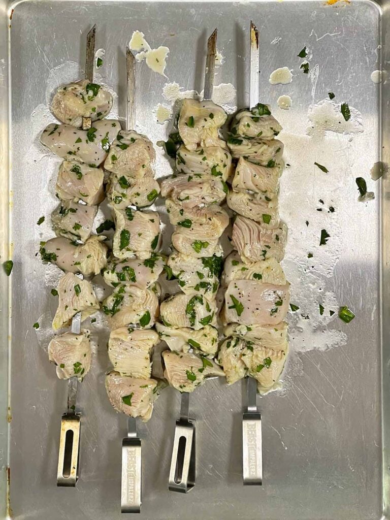 Raw chicken skewers on a prep sheet.