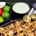 Cilantro lime grilled chicken skewers on a dark plate with vegetables and dip in the background.
