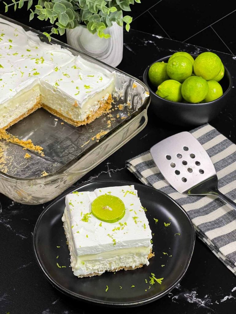 A slice of key lime lush on a round plate garnished with a lime slice and zest.