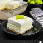 A slice of key lime lush on a round plate garnished with a lime slice and zest.