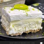 A slice of key lime lush on a round plate garnished with a lime slice and zest.