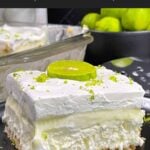 A slice of key lime lush on a round plate garnished with a lime slice and zest.
