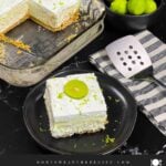 A slice of key lime lush on a round plate garnished with a lime slice and zest.