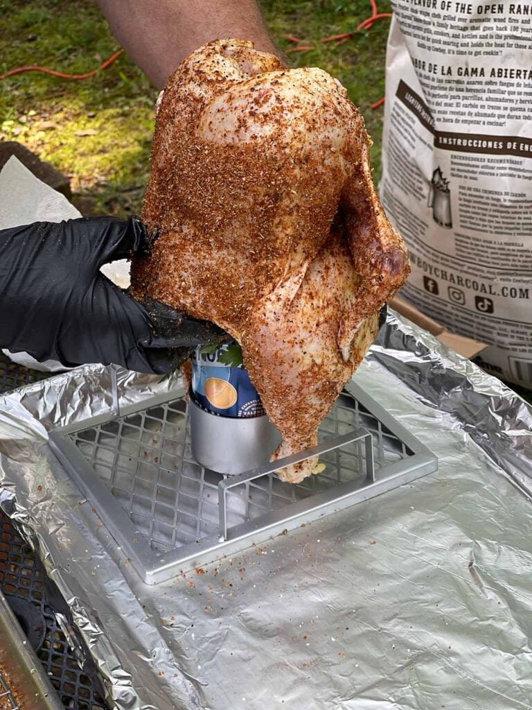 Putting a seasoned raw chicken onto a beer can stand.