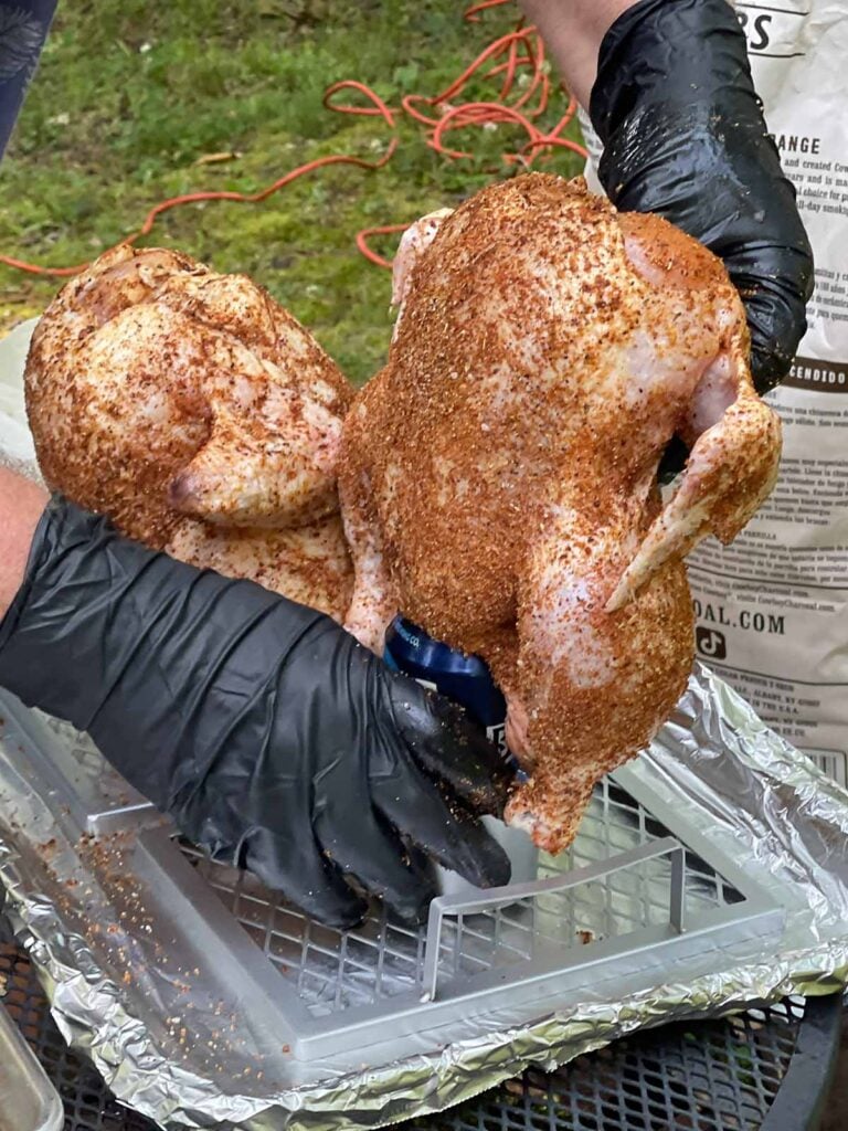Putting a seasoned raw chicken onto a beer can stand.