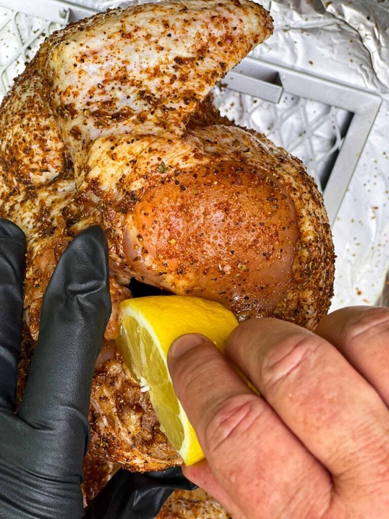 Closing the opening on a raw chicken with a cut lemon.
