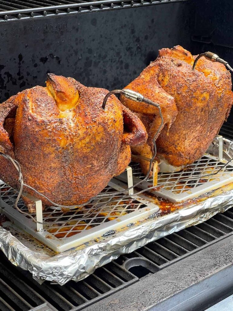 Two smoked chickens on a beer can stands in a smoker.