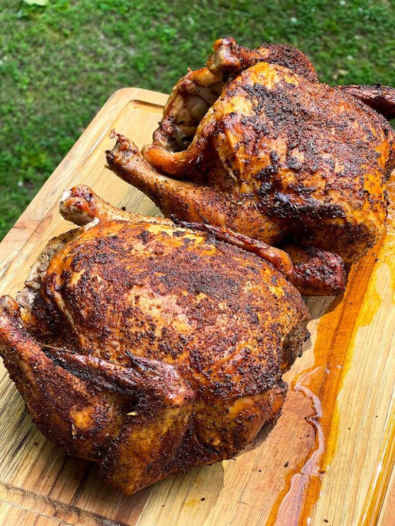 Two smoked chickens on a wooden cutting board.