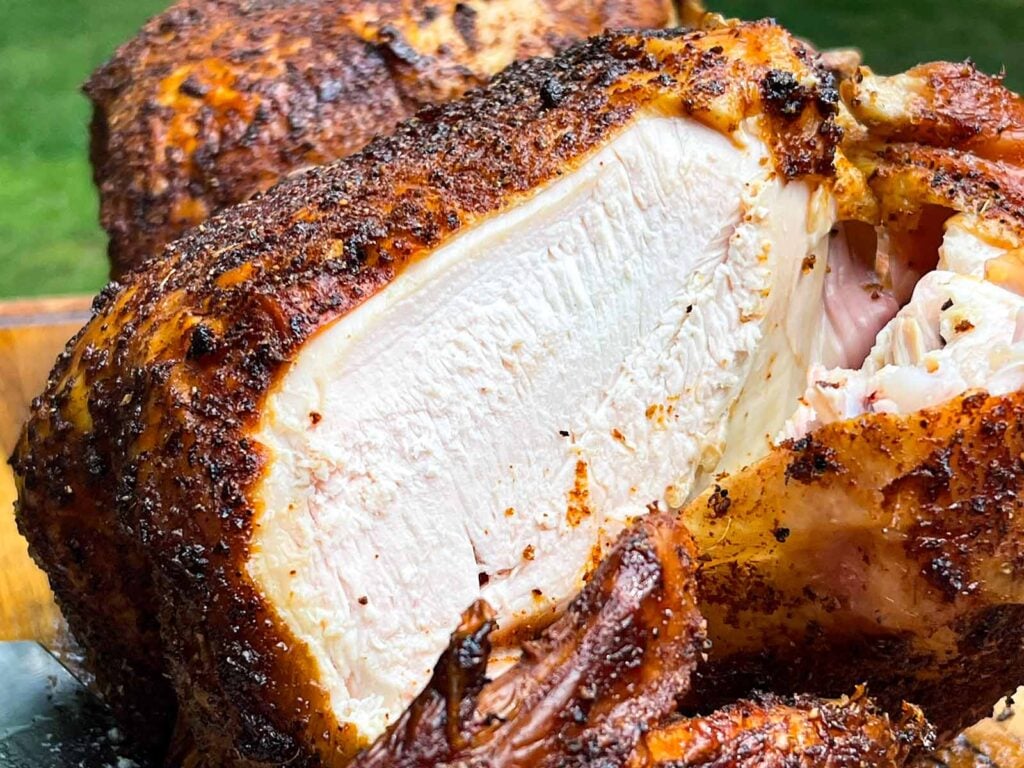 Smoked beer can chicken with a slice cut off showing the white meat.