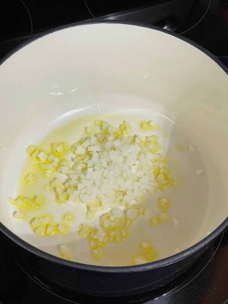 Diced onions cooking in olive oil in a Dutch oven.