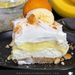A slice of banana pudding lush on a dark plate garnished with crushed vanilla wafers.