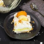 A slice of banana pudding lush on a dark plate garnished with crushed vanilla wafers.