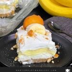 A slice of banana pudding lush on a dark plate garnished with crushed vanilla wafers.