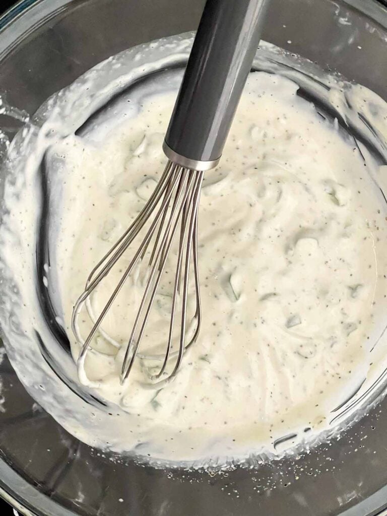 Mayonnaise, dill pickle juice, green onions, garlic powder, kosher salt, and black pepper whisked together in a glass mixing bowl.