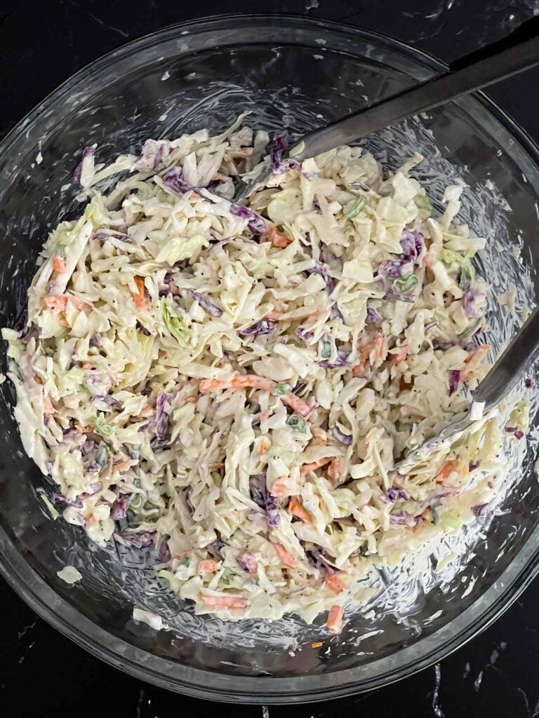 Coleslaw mix being tossed with the creamy homemade dressing until evenly coated.