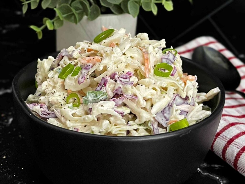Bowl of Classic Coleslaw with crisp cabbage, carrots, and green onions in a creamy homemade dressing.