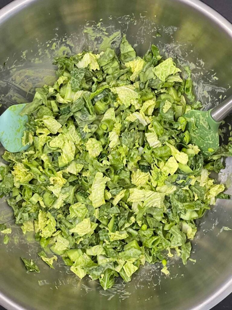 Green Goddess Salad tossed with the dressing in a large metal bowl.