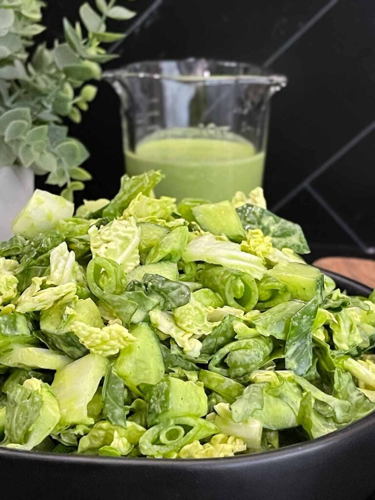 Green Goddess Salad served in a black bowl with Napa cabbage, spinach, arugula, cucumbers, snow peas, and creamy herb dressing.