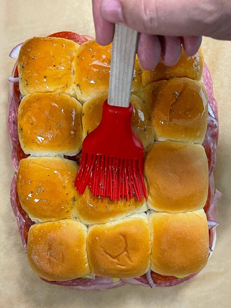 Brushing butter on top of Hawaiian rolls.