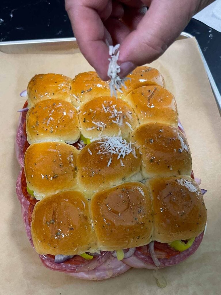 Sprinkling cheese on top of sliders
