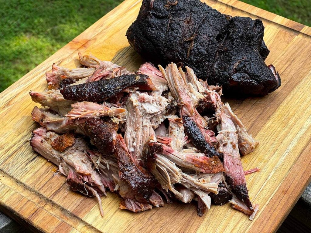 Smoked boneless pork butt pulled apart on a wooden cutting board with a dark, smoky bark.