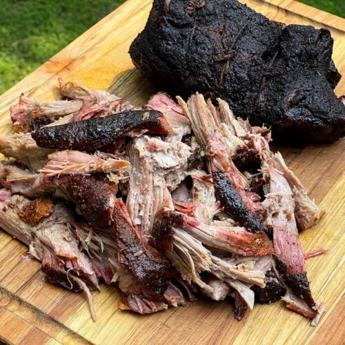 Smoked boneless pork butt pulled apart on a wooden cutting board with a dark, smoky bark.