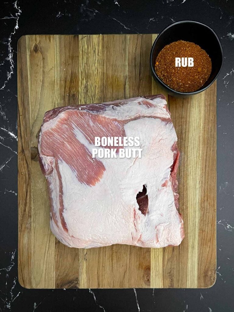 Whole boneless pork butt on a wooden cutting board with homemade BBQ rub in a black bowl.