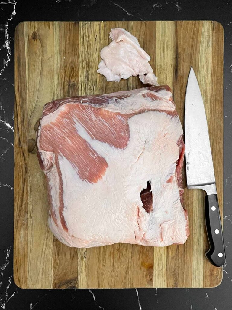 Boneless pork butt on a wooden cutting board with excess fat trimmed away before smoking.