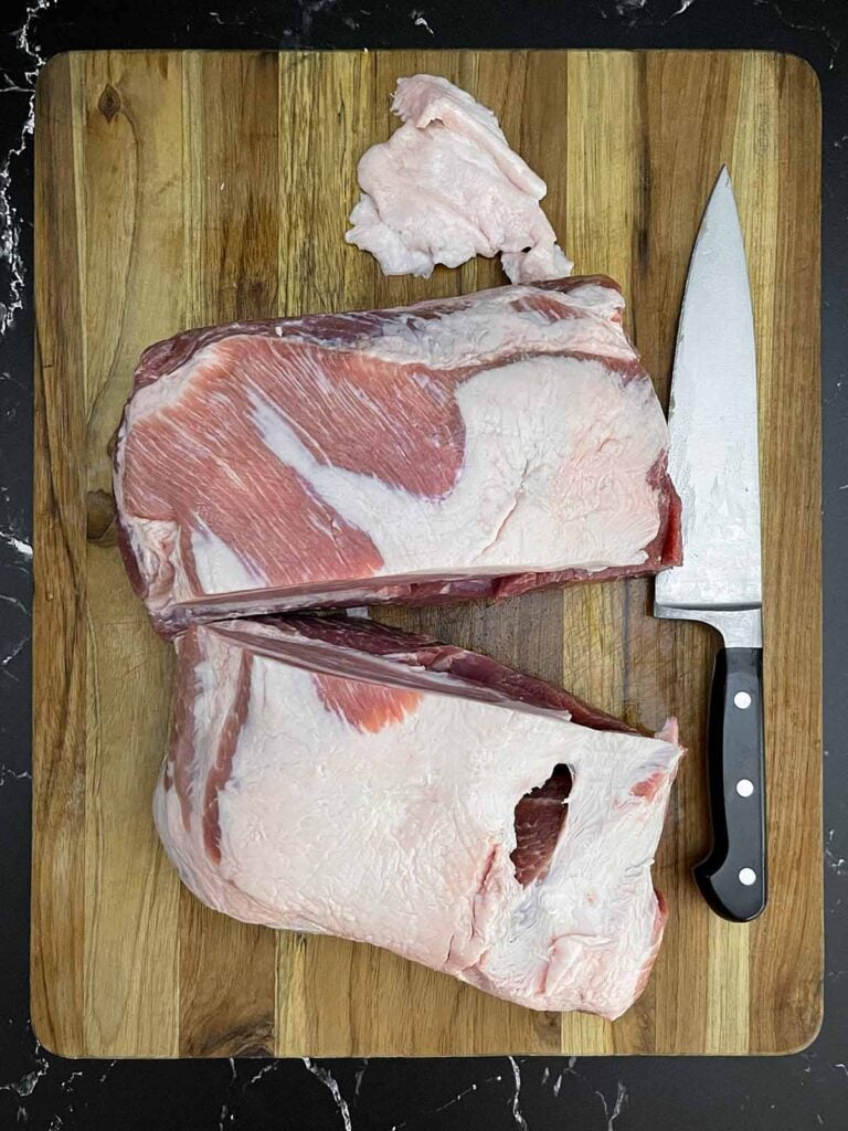 Boneless pork butt cut into two equal pieces on a wooden cutting board.