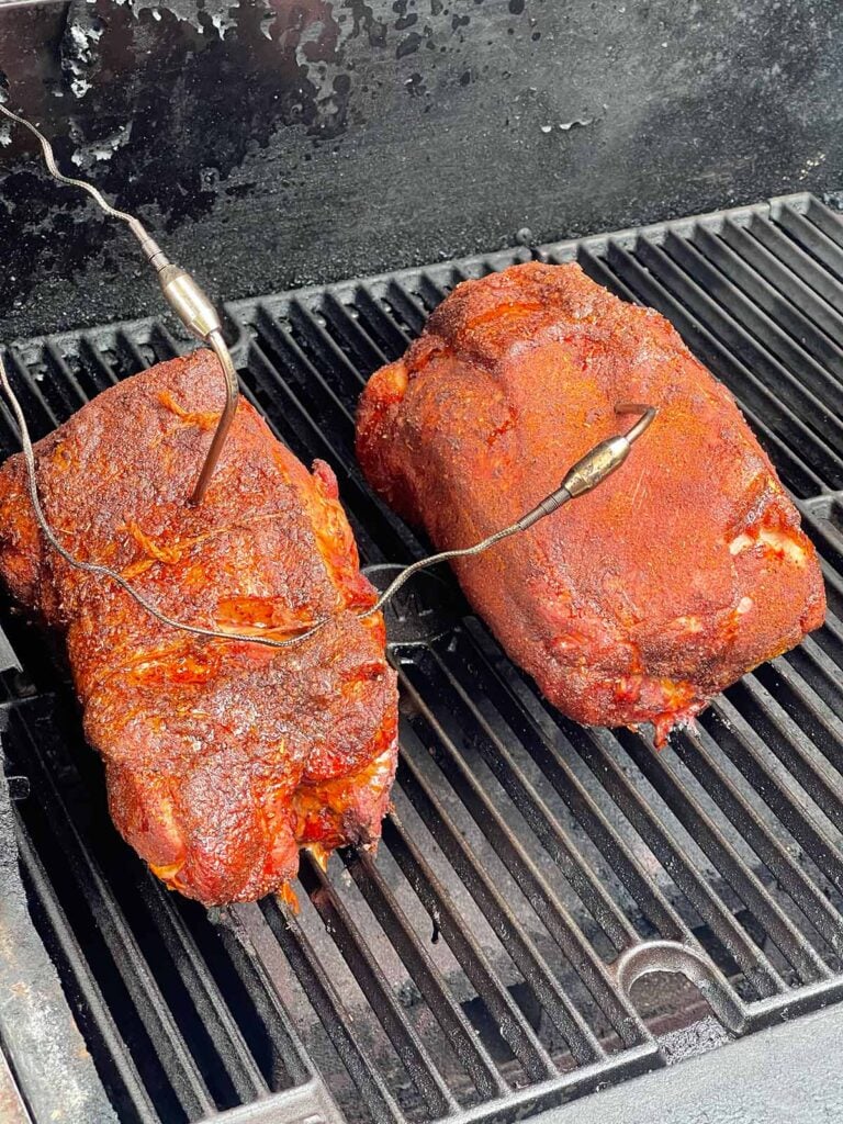 Boneless pork butt halves developing a rich bark after a few hours in the smoker.