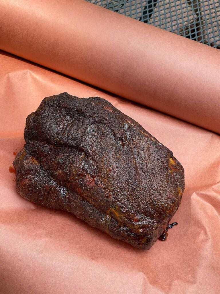 Smoked boneless pork butt resting on pink butcher paper before wrapping.