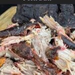 One smoked pork butt pulled apart beside the remaining whole half on a wooden cutting board.